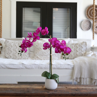 Realistic faux purple Phalaenopsis orchid with vibrant blooms and lush green leaves on tall stem